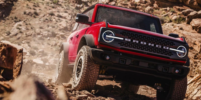 Red Ford Bronco off-roading on a rugged, rocky trail, angled front view.