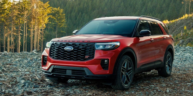 Red Ford Explorer ST SUV parked on a rocky trail with a forest and trees in the background.