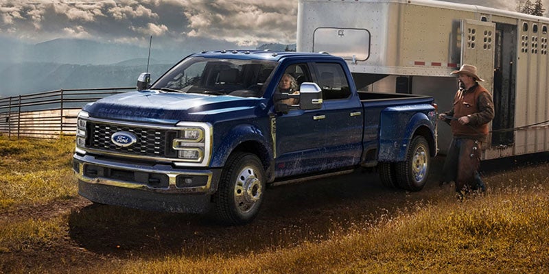 Blue Ford Super Duty dually truck with a horse trailer, a driver, and a rancher next to it, in a rural mountain setting.
